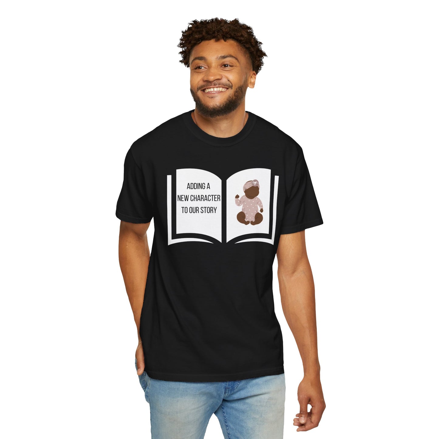 Black t-shirt featuring an open book graphic with the text "Adding a New Character to Our Story" and an image of a crib/baby booties/teddy bear, symbolizing a pregnancy announcement.