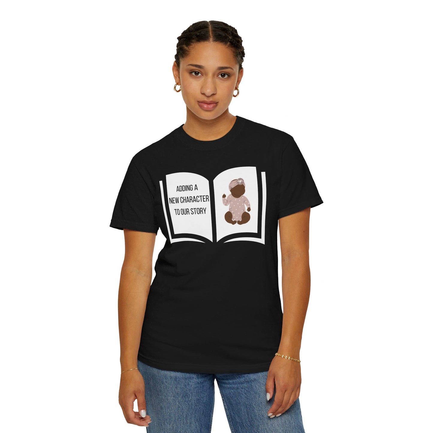 Black t-shirt featuring an open book graphic with the text "Adding a New Character to Our Story" and an image of a crib/baby booties/teddy bear, symbolizing a pregnancy announcement.