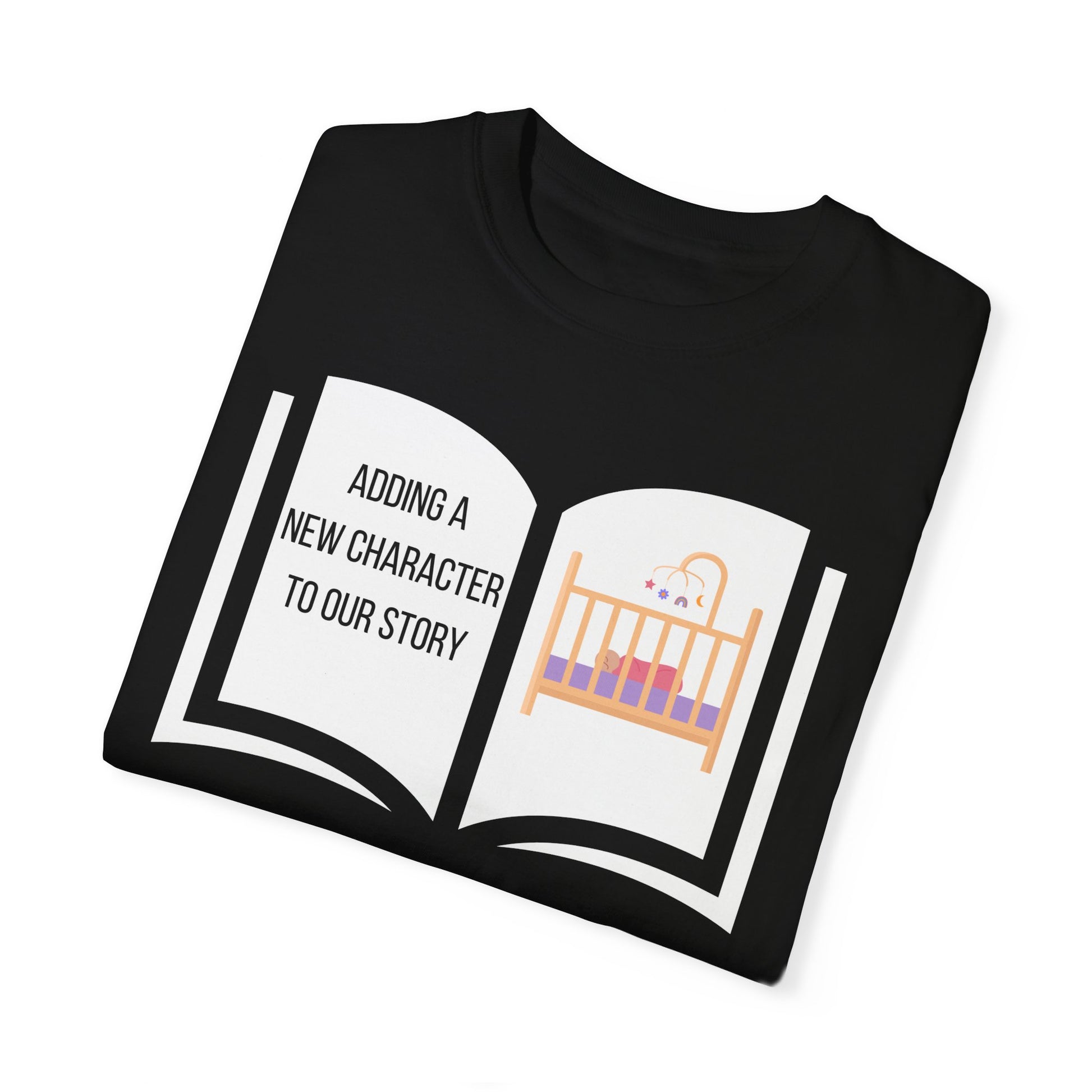 Black t-shirt featuring an open book graphic with the text "Adding a New Character to Our Story" and an image of a crib/baby booties/teddy bear, symbolizing a pregnancy announcement.