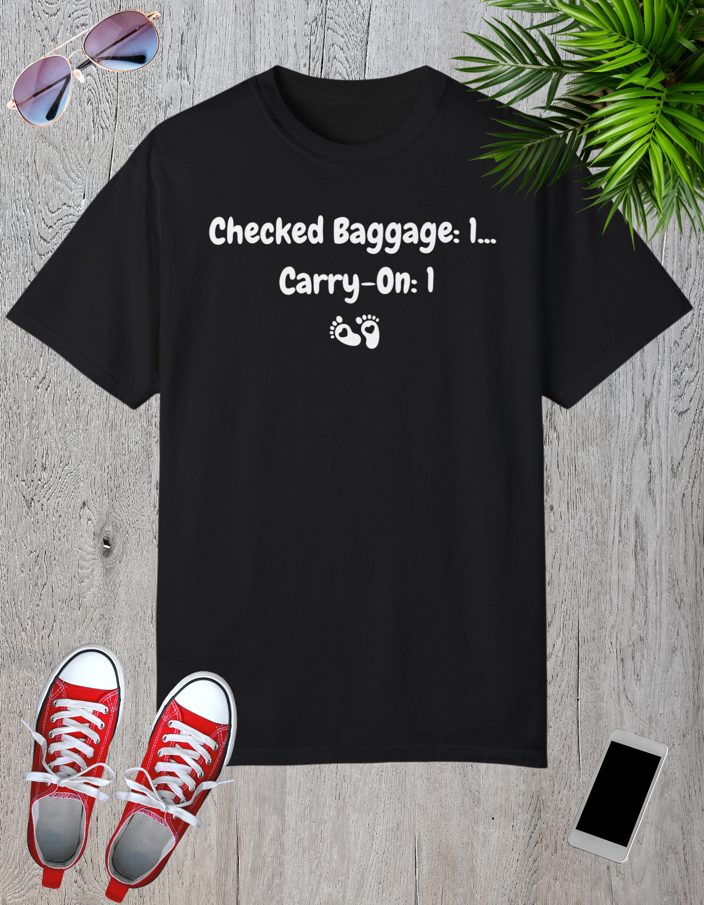 Cream-colored t-shirt featuring a playful design with the text "Checked Baggage: 1... Carry-On: 1" and tiny baby footprints.