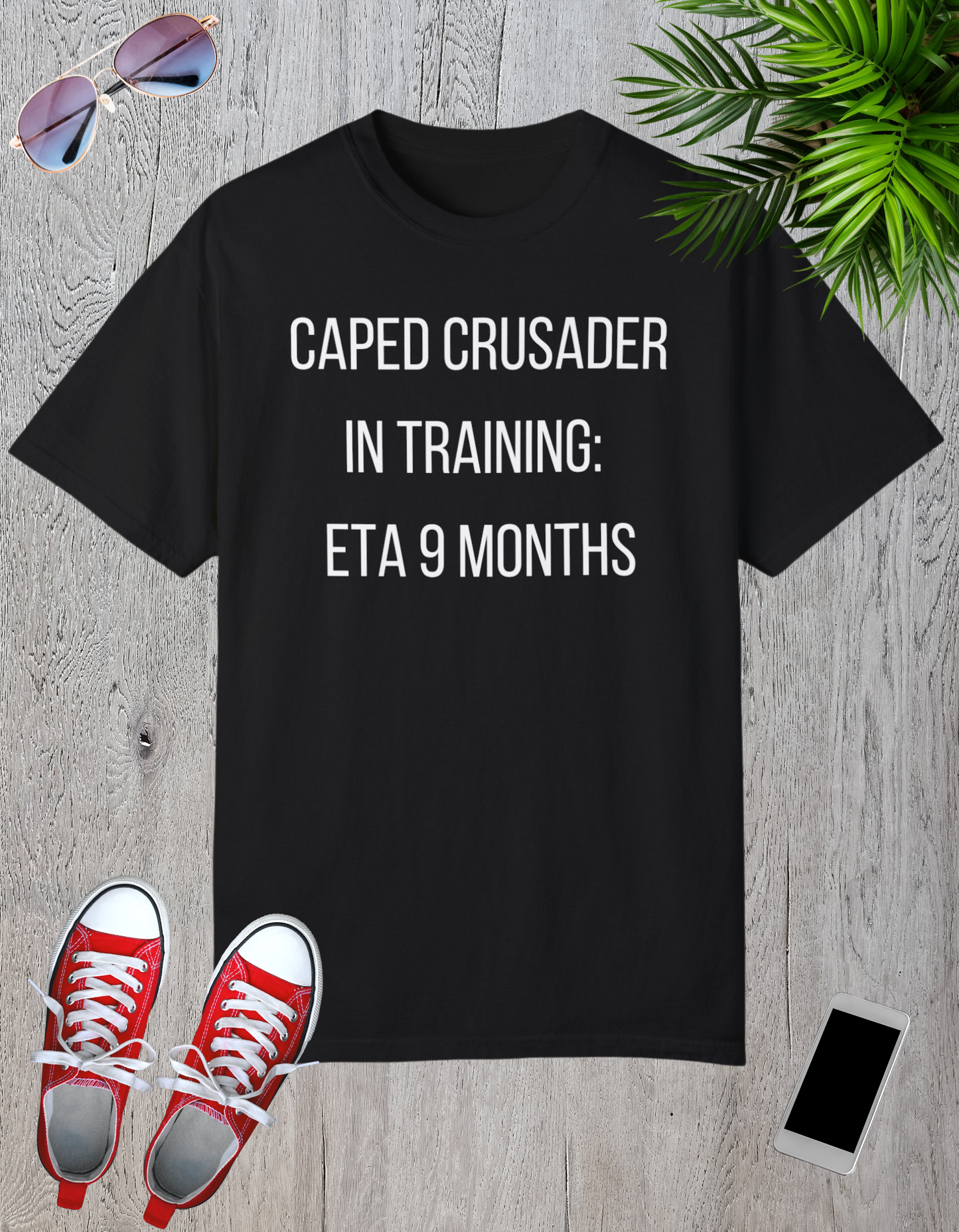 Black t-shirt with the text "Caped Crusader in Training: ETA 9 Months" in a playful superhero-themed font.