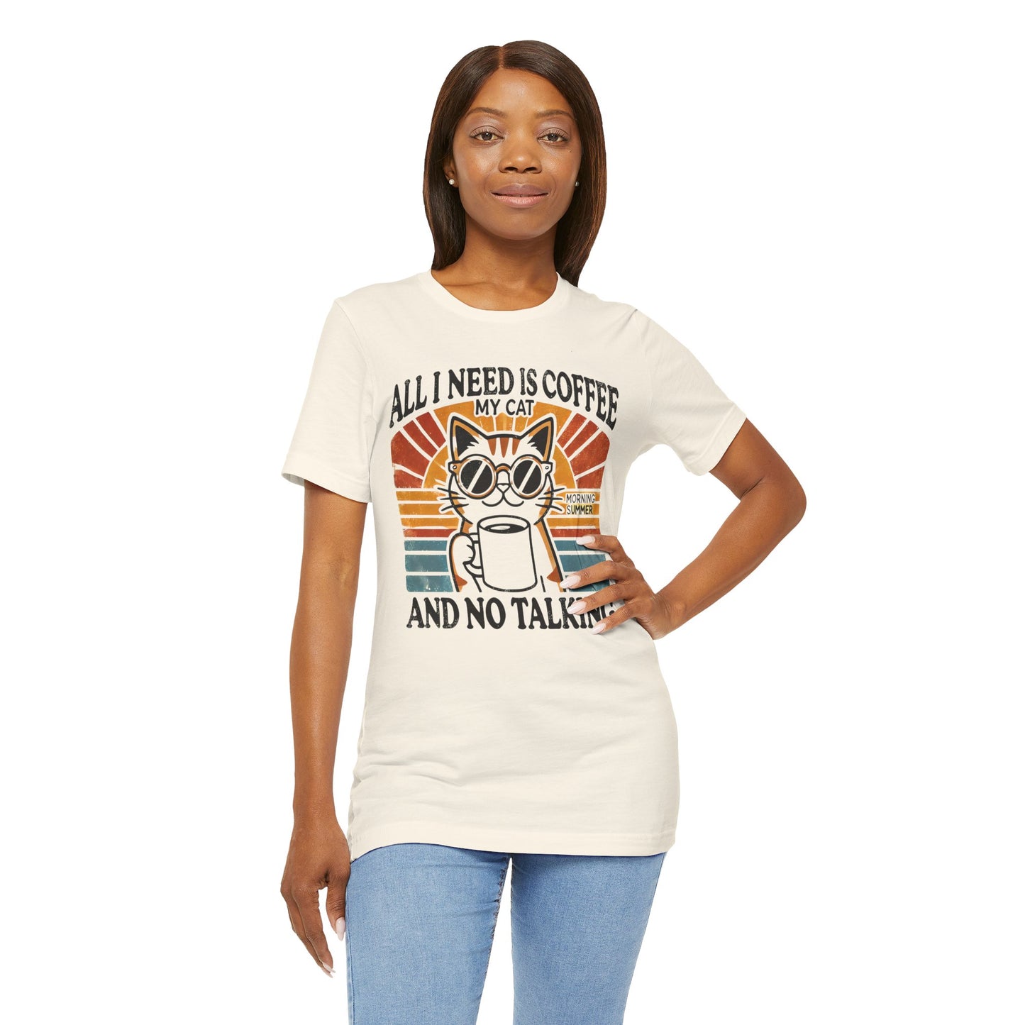 A light-colored t-shirt with a retro design of a cat wearing sunglasses, holding a coffee cup, and the text "All I Need is Coffee and My Cat.