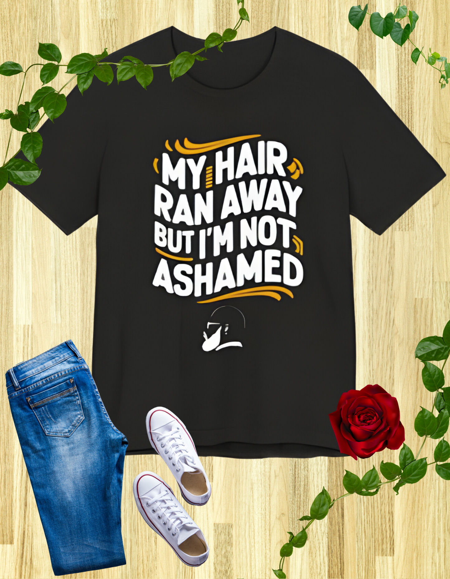 A  t-shirt with the text "My Hair Ran Away But I'm Not Ashamed" in bold white and yellow letters, accompanied by a playful illustration of a bald head with a smile.