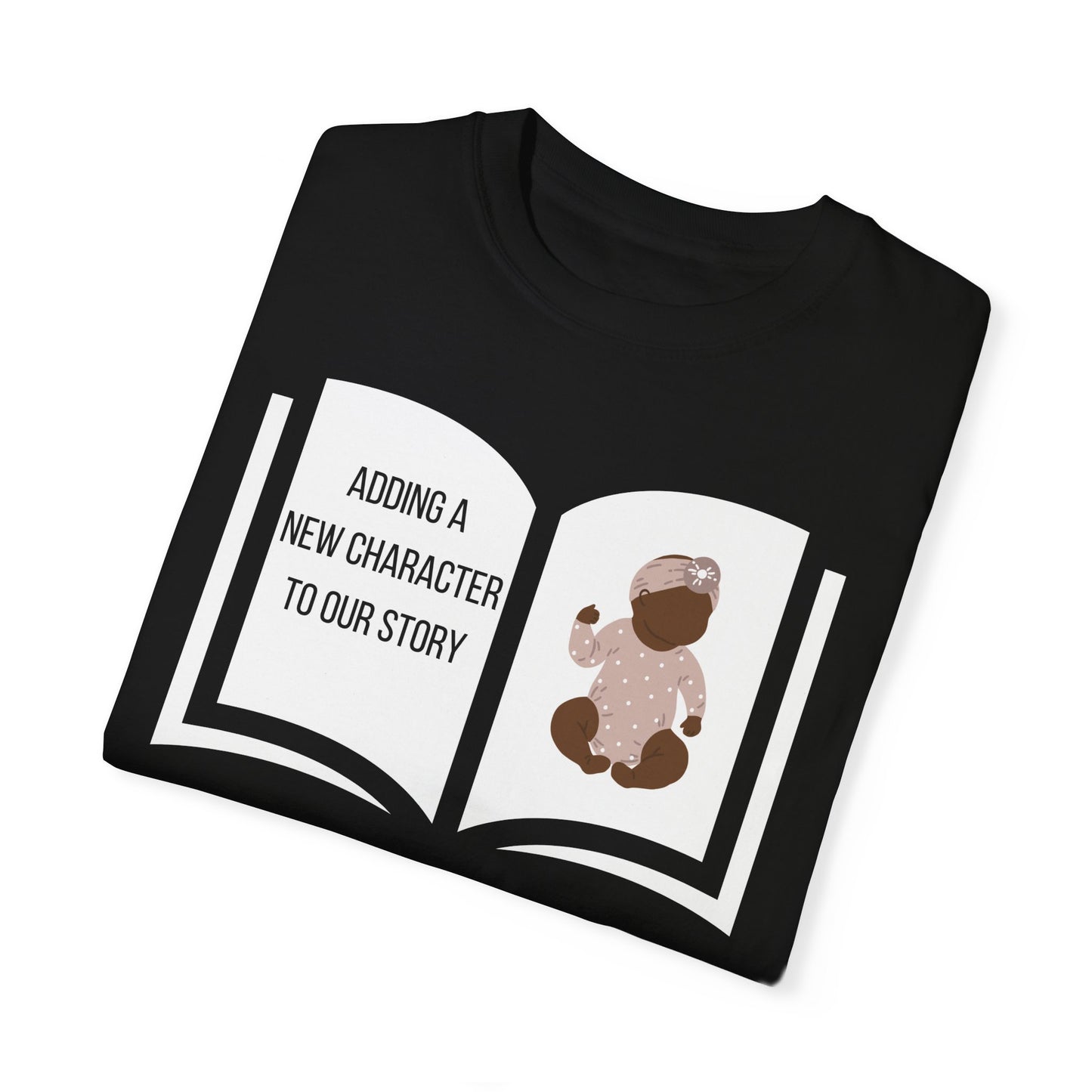 Black t-shirt featuring an open book graphic with the text "Adding a New Character to Our Story" and an image of a crib/baby booties/teddy bear, symbolizing a pregnancy announcement.