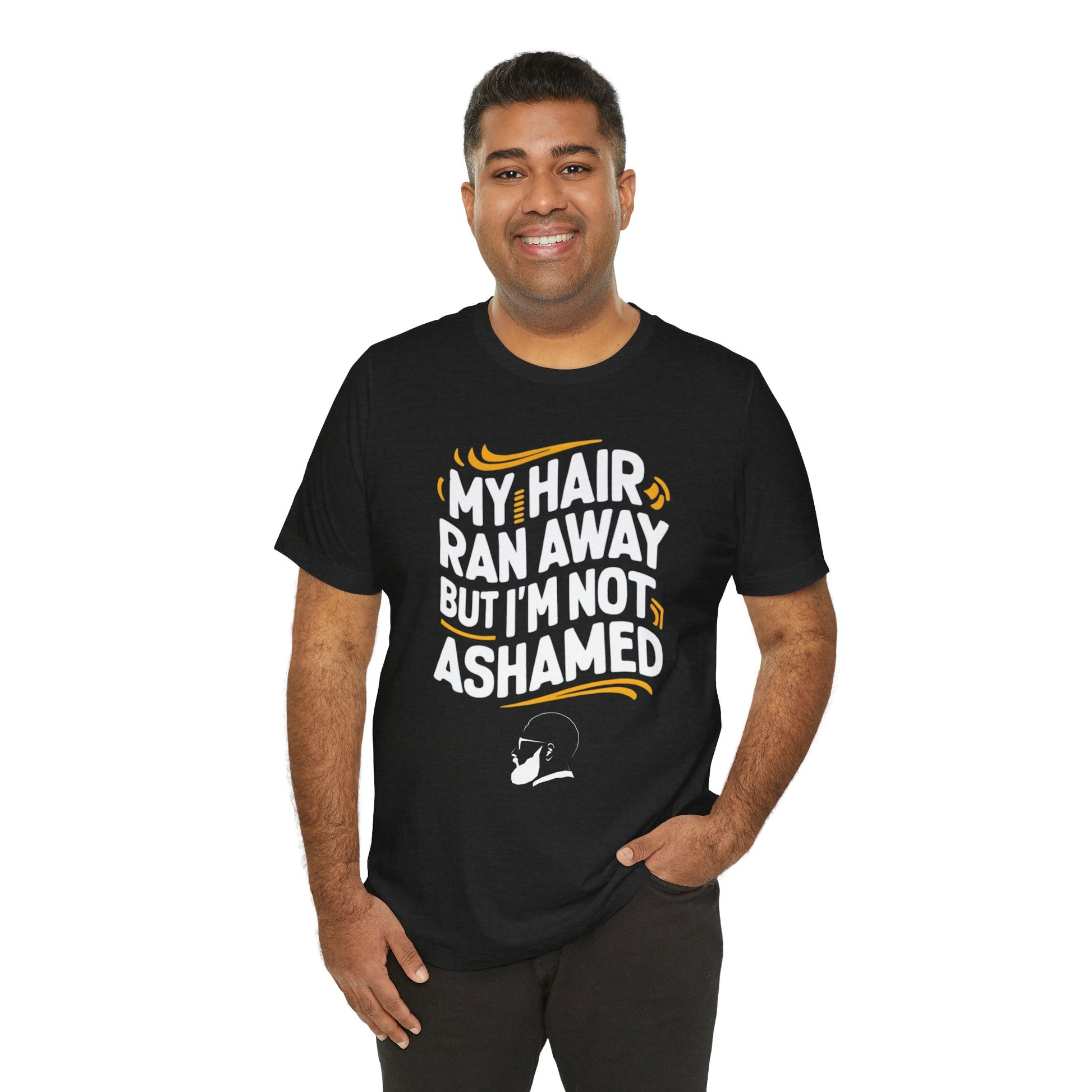 A  t-shirt with the text "My Hair Ran Away But I'm Not Ashamed" in bold white and yellow letters, accompanied by a playful illustration of a bald head with a smile.