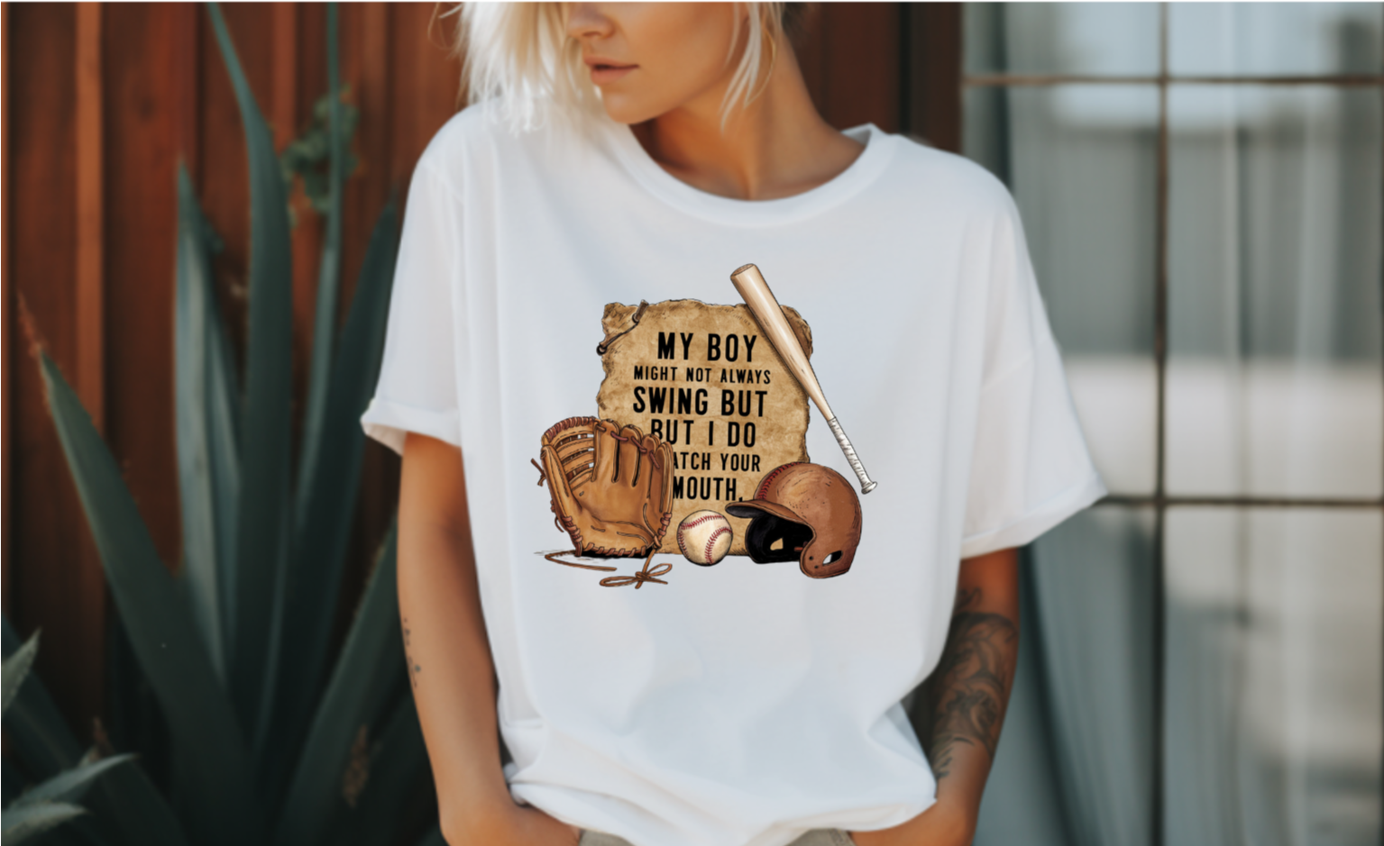 A t-shirt with a vintage-style baseball graphic featuring a baseball bat, glove, and helmet.  The text "My Boy Might Not Always Swing But I Do So Watch Your Mouth" is written in white above the graphic.