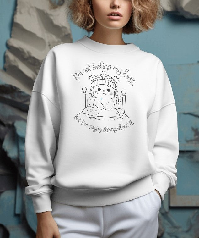 Adorable white sweatshirt with a line-art illustration of a bear in bed, with text 'I'm not feeling my best' and 'but I'm staying strong about it.'